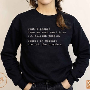 May include: Black sweatshirt with white text that reads "Just 8 people have as much wealth as 3.6 billion people. People on welfare are not the problem."