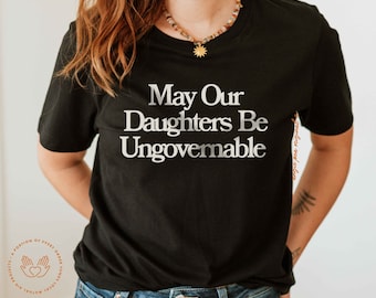 Może przedstawiać: Czarny T-shirt z nadrukiem "May Our Daughters Be Ungovernable" w kolorze białym na przodzie.