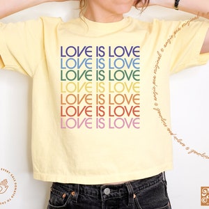 May include: A yellow cropped t-shirt with the phrase "LOVE IS LOVE" repeated in rainbow colors.