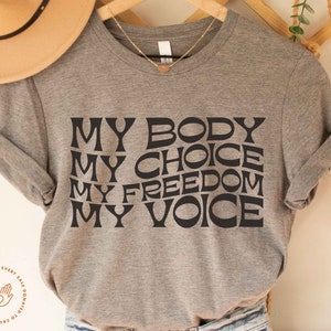 May include: Gray t-shirt with the text "MY BODY MY CHOICE MY FREEDOM MY VOICE" in black stylized lettering.