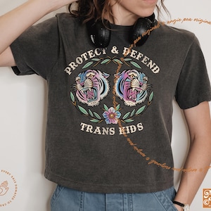 May include: A dark gray t-shirt with a graphic of two colorful tigers with the text "Protect & Defend Trans Kids".