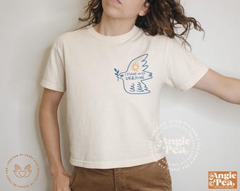 May include: A white t-shirt with a blue and yellow graphic of a dove with an olive branch and the text "I stand with Ukraine".