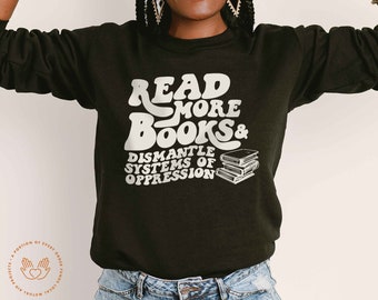 May include: Black sweatshirt with white text that reads "Read More Books & Dismantle Systems of Oppression". The text is in a retro font. There are three stacked books in the image.