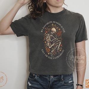 May include: A dark gray t-shirt with a skeleton graphic and the text "My favorite season is the fall of the patriarchy".