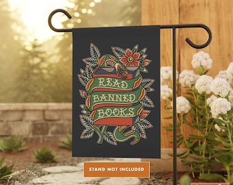 May include: A garden flag with a black background featuring a vintage tattoo style illustration of a book with a snake wrapped around it. The book has a red ribbon with the text "Read Banned Books" in white. The flag is surrounded by green leaves and a red flower.