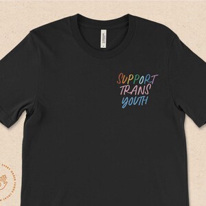 May include: Black t-shirt with the text "SUPPORT TRANS YOUTH" in rainbow colors.