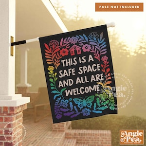 May include: A black garden flag with a rainbow floral border and the text "This is a safe space and all are welcome".