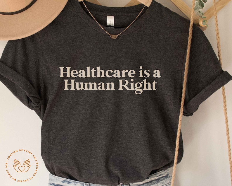 May include: A dark grey t-shirt with the text "Healthcare is a Human Right" printed in white. A portion of every sale is donated to causes we fight for.