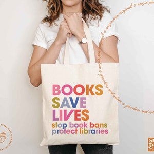 Puede incluir: Una bolsa de tela blanca con el texto "BOOKS SAVE LIVES stop book bans protect libraries" en letras de colores. La bolsa est&aacute; siendo sostenida por una persona.