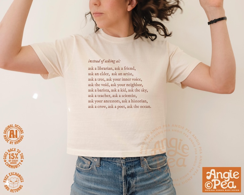 May include: Cream-colored t-shirt with the text "instead of asking ai: ask a librarian...ask the ocean." The shirt has a crew neck and short sleeves. The design includes a circular logo and text at the bottom.