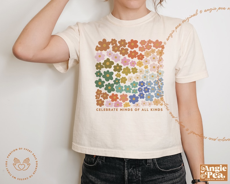 May include: A cream-colored cropped t-shirt with a graphic of colorful flowers arranged in a rainbow pattern. The text "Celebrate Minds of All Kinds" is printed below the flowers.