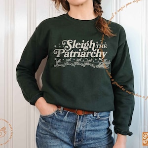 May include: A dark green sweatshirt with a white graphic print that says "Sleigh the Patriarchy" with a stylized image of reindeer pulling a sleigh.