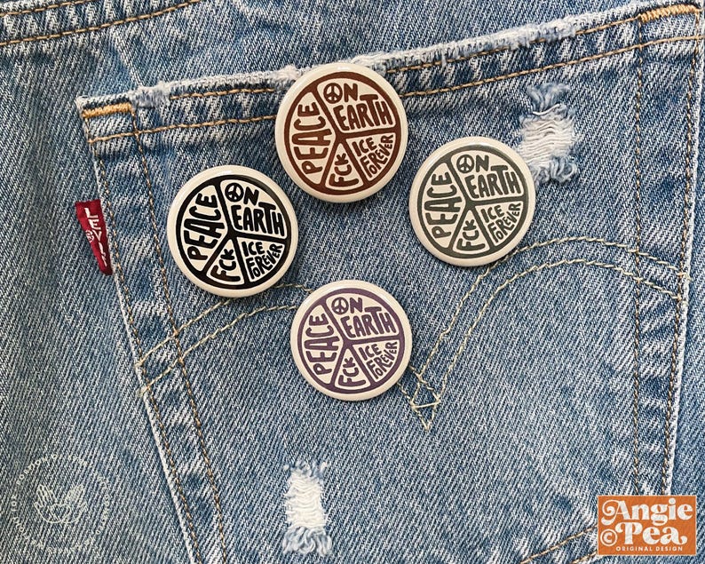 May include: Four round buttons with a peace symbol design, featuring the words "Peace," "On Earth," and "Ice Fck Forever." The buttons are in shades of black, brown, and purple, set against a denim background.