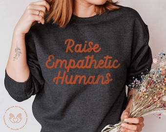 May include: A dark grey sweatshirt with the text "Raise Empathetic Humans" printed in orange on the front.