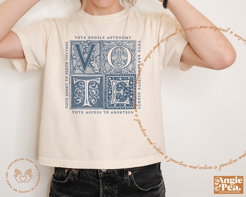 May include: A cream-colored t-shirt with a blue graphic of the word "VOTE" in a vintage style font. The graphic is made up of four squares, each with a different design. The text "VOTE RIGHT TO BIRTH CONTROL", "VOTE BODILY AUTONOMY", "VOTE REPRODUCTIVE RIGHTS", and "VOTE ACCESS TO ABORTION" surrounds the graphic.