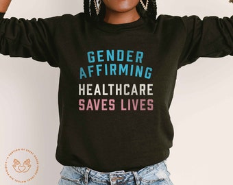 May include: Black sweatshirt with the text "Gender Affirming Healthcare Saves Lives" in blue, white, and pink lettering.