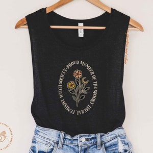 K&ouml;nnte beinhalten: Schwarzes &auml;rmelloses Tanktop mit einem wei&szlig;en Kreis-Motiv mit einem Blumendesign und dem Text "Feminist Witch Society, Proud Member of the Spooky Liberal"