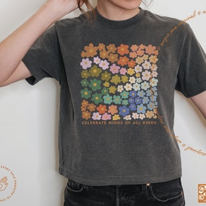 May include: A dark gray t-shirt with a colorful floral design and the text "Celebrate Minds of All Kinds".