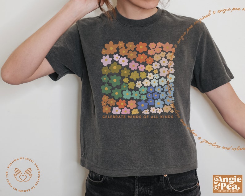 May include: A dark gray t-shirt with a colorful floral design and the text "Celebrate Minds of All Kinds".