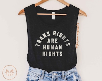 May include: Black tank top with the text "TRANS RIGHTS ARE HUMAN RIGHTS" in white lettering. The tank top is hanging on a wooden hanger.