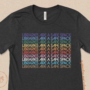 May include: A dark grey t-shirt with the text "LIBRARIES ARE A SAFE SPACE" repeated in rainbow colors.