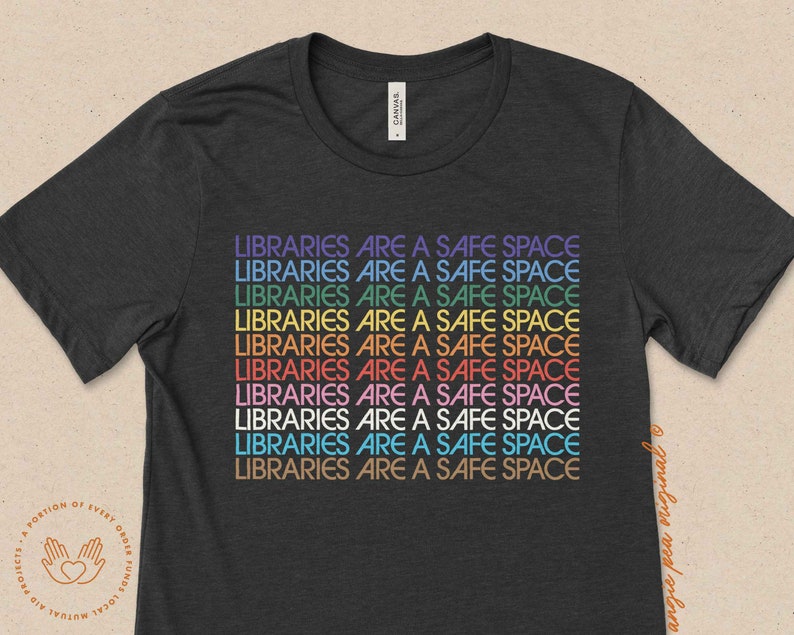 May include: A dark grey t-shirt with the text "LIBRARIES ARE A SAFE SPACE" repeated in rainbow colors.