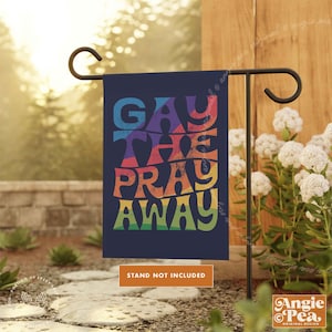 May include: A blue garden flag with the text "Gay The Pray Away" in rainbow colors. The text is in a retro font style. The flag is hanging on a black metal stand. The text "Stand Not Included" is printed below the flag.