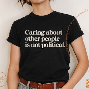 May include: A black t-shirt with white text that reads "Caring about other people is not political."