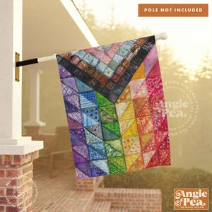 May include: A colorful, rainbow-themed garden flag with a patchwork quilt design. The flag is made of fabric and has a white background with a variety of colored squares and triangles. The flag is hanging from a pole and is blowing in the wind.