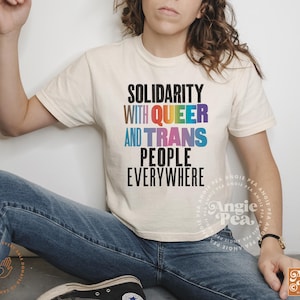 May include: A white t-shirt with the text "Solidarity with Queer and Trans People Everywhere" in rainbow colors. The text is in a bold, blocky font.