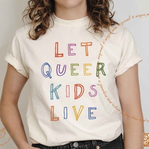 May include: A white t-shirt with the text "Let Queer Kids Live" printed in rainbow colors. The text is in a hand-drawn style.