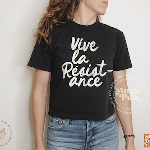 May include: A black cropped t-shirt with the text "Vive la Resist-ance" in white lettering. The shirt is being worn by a person with long brown hair.