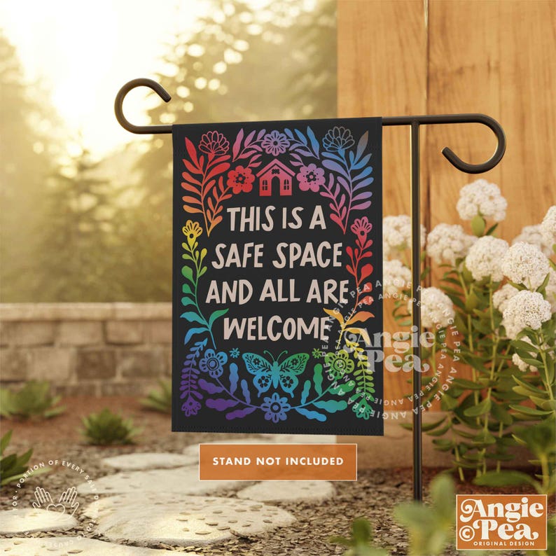 May include: A black garden flag with a rainbow floral design and the text "This is a safe space and all are welcome".