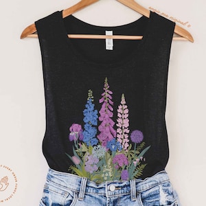 Puede incluir: Un top negro de tirantes con un estampado floral con flores moradas, azules y rosas. Las flores est&aacute;n dispuestas en forma de ramo y se centran en la parte delantera del top.