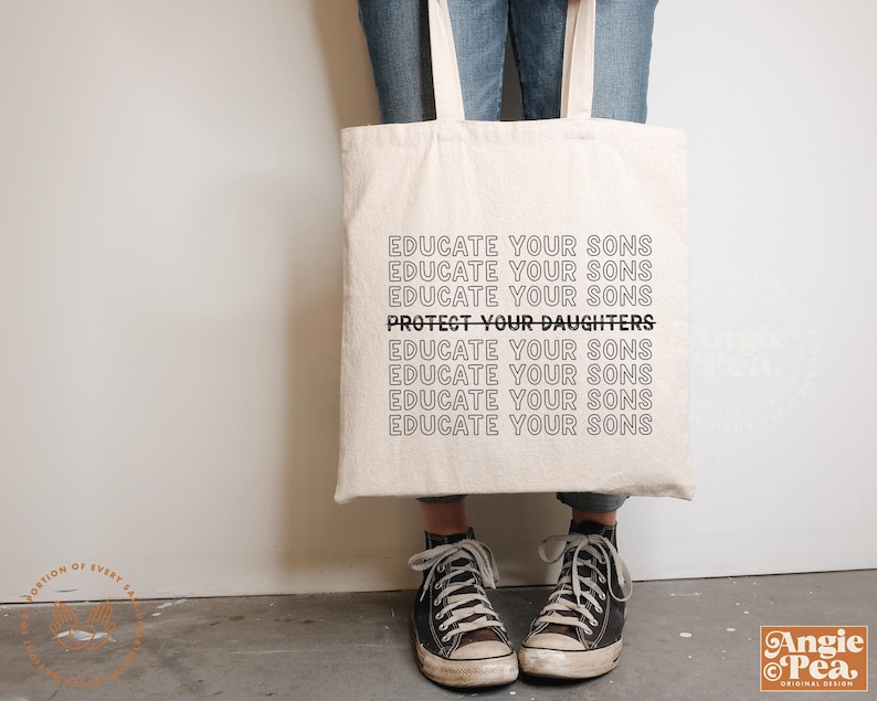 Op de afbeelding: Een witte tote bag met de tekst "Educate your sons" die meerdere keren wordt herhaald, met de zin "Protect your daughters" in vetgedrukte letters in het midden van de tas.