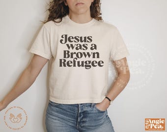 May include: A white cropped t-shirt with the text "Jesus was a Brown Refugee" printed in brown letters.