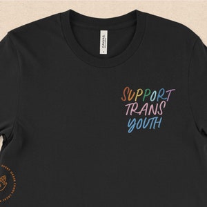 以下が含まれることがあります： レインボーカラーで「SUPPORT TRANS YOUTH」と書かれた黒いTシャツです。