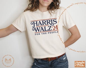 May include: A white t-shirt with a blue and red graphic that says "HARRIS WALZ '24 FOR THE PEOPLE".