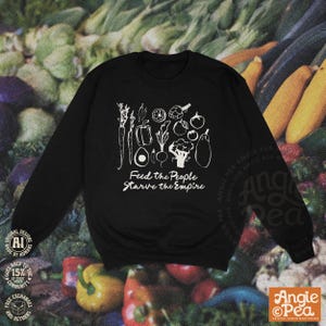 May include: A black long-sleeve sweatshirt featuring a white graphic print of various vegetables including a carrot, pepper, avocado, and broccoli, with the text "Feed the People Starve the Empire" printed in white below the produce illustrations.