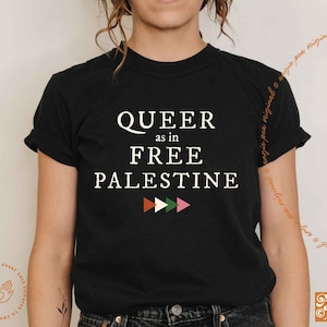 May include: Black t-shirt with white text that reads "QUEER as in FREE PALESTINE" with a row of three colorful triangles below the text.