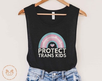 Peut inclure: Un débardeur noir avec un arc-en-ciel et le texte "PROTECT TRANS KIDS" imprimé sur le devant. L'arc-en-ciel est dans des tons de rose, bleu et blanc avec un cœur rose au centre.