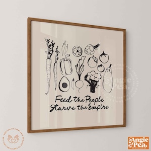 May include: A framed print featuring a collection of sketched vegetables in black ink on a cream background. The text "Feed the People, Starve the Empire" is written below the illustrations. The frame is a light brown color.