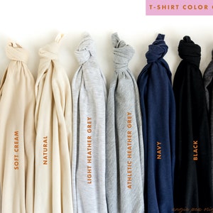 K&ouml;nnte beinhalten: Ein Farbf&uuml;hrer f&uuml;r T-Shirts, der verschiedene Stoffschattierungen zeigt. Das Bild zeigt gefaltete T-Shirts in Farben wie Wei&szlig;, Soft Cream, Natur, Hellgrau, Athletic Heather Grey, Marine, Schwarz und Dunkelgrau. Text kennzeichnet jede Farbe.