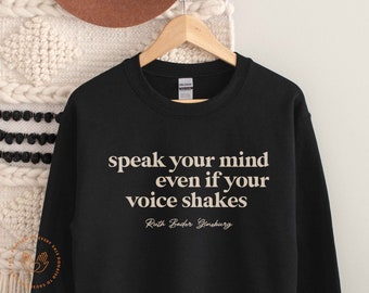 May include: Black sweatshirt with the quote "speak your mind even if your voice shakes" in beige text, attributed to Ruth Bader Ginsburg.