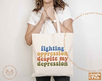 May include: A cream-colored canvas tote bag featuring the text "fighting oppression despite my depression" printed in four stacked rows of wavy, retro-style lettering in blue, yellow, orange, and green colors with two sturdy fabric handles.