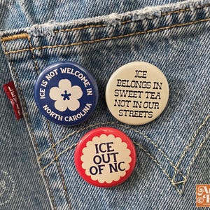 May include: Three round pinback buttons with text and graphics are displayed on a denim background. The buttons have the phrases "ICE IS NOT WELCOME IN NORTH CAROLINA", "ICE BELONGS IN SWEET TEA NOT IN OUR STREETS", and "ICE OUT OF NC".