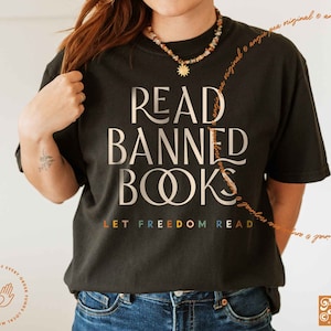 May include: A black t-shirt with the text "READ BANNED BOOKS" in gold lettering. The text "LET FREEDOM READ" is printed below in rainbow colors.