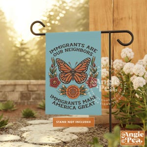 May include: A teal garden flag with the text "IMMIGRANTS ARE OUR NEIGHBORS" and "IMMIGRANTS MAKE AMERICA GREAT". It features a monarch butterfly and floral designs. The flag is displayed on a black metal stand.