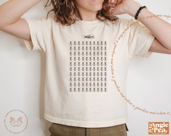 Può includere: Una maglietta bianca con una grafica di una griglia di formiche e un singolo grillo al centro. Il testo "Angie Pea Original" è scritto sul lato della maglietta.