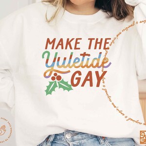 May include: White sweatshirt with the text "MAKE THE YULETIDE GAY" in rainbow colors with a green holly sprig underneath. The text is in a retro font.